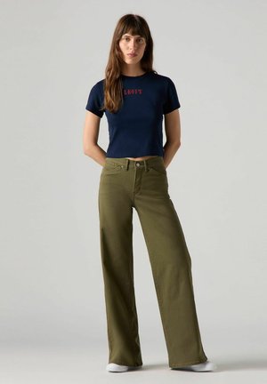 Marineblå cropped t-shirt med rød "LEVI'S" tekst, parret med vidde bukser i olivengrøn, som har forlommer og en struktureret stof. Hvide sneakers.