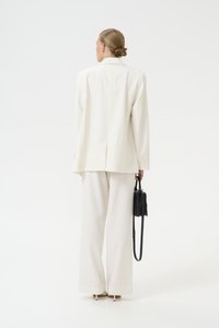 White pinstriped suit made of light fabric, featuring a loose-fitting blazer and wide-leg trousers, complemented by a small black handbag.