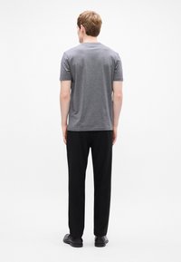 Γκρι μπλούζα με στρογγυλή λαιμόκοψη, συνδυασμένη με μαύρο παντελόνι σε χαλαρή γραμμή. Το ύφασμα φαίνεται λείο. Τα παπούτσια είναι μαύρα, με απλό σχέδιο και χαμηλό προφίλ.