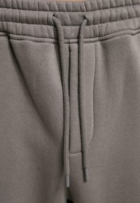 Grå joggebukser med elastisk midjebånd, strammesnor og en glatt tekstur med sidelommer.