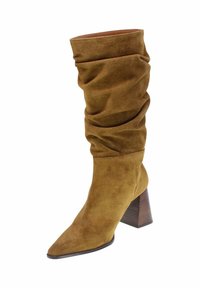 Bota de ante marrón hasta la rodilla con diseño holgado, puntera afilada y tacón de madera apilada. Textura suave y pliegues relajados.