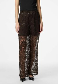 Brown lace wide-leg pants with a sheer design, featuring floral patterns and sparkling accents, paired with a black top and heels.