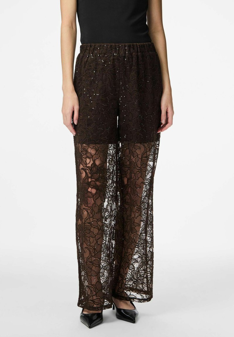 Brown lace wide-leg pants with a sheer design, featuring floral patterns and sparkling accents, paired with a black top and heels.