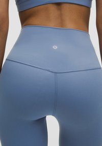 Vysoké legíny svetlo modrej farby s hladkou textúrou a minimálnym švom. Obsahujú malé logo na zadnom páse.