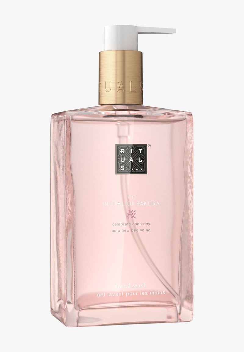 Klare rechteckige Flasche mit rosa Flüssigkeit. Verfügt über eine goldfarbene Kappe und einen Pumpspender. Text enthält "The Ritual of Sakura" und "Handseife."