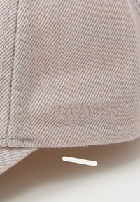Beige denim cap featuring an embroidered "Levi's" logo. The design includes a structured brim and a textured fabric surface.