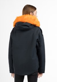 Parka blu scuro con un ampio colletto in pelliccia sintetica arancione brillante, cappuccio e dettagli con bottoni laterali. Tessuto testurizzato offre calore e durata.