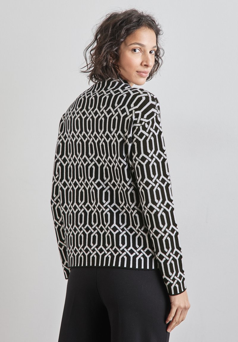 Pull en noir et blanc avec des motifs géométriques, manches longues, bord côtelé et une silhouette ajustée. Fabriqué en tissu tricoté.