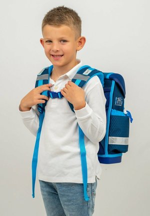 Zaino blu e navy con tessuto a fantasia, spallacci regolabili e dettagli riflettenti. Il bambino aggiusta la fibbia sul petto, indossando una maglietta bianca.