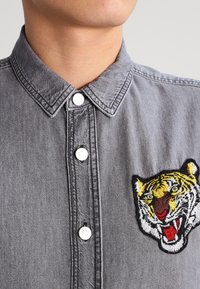Grijze denim overhemd met een gestructureerde kraag, voorzien van witte knopen en een opvallend geborduurd tijgerhoofd op de linkerkant van de borst.