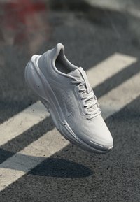 White sneaker with a mesh upper, rounded toe, and prominent lacing system. Features a textured sole and subtle logo detailing.