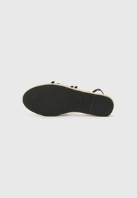 Suela de sandalia negra con una suela exterior de goma texturizada y una entresuela de yute de color claro. Presenta rayas verticales a lo largo de la plantilla.