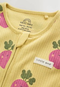 Žltý žebrovaný detský odev s ružovými usmievajúcimi sa reďkovkami a štítkom s nápisom "little one" pri výstrihu a zapínaním na zips.