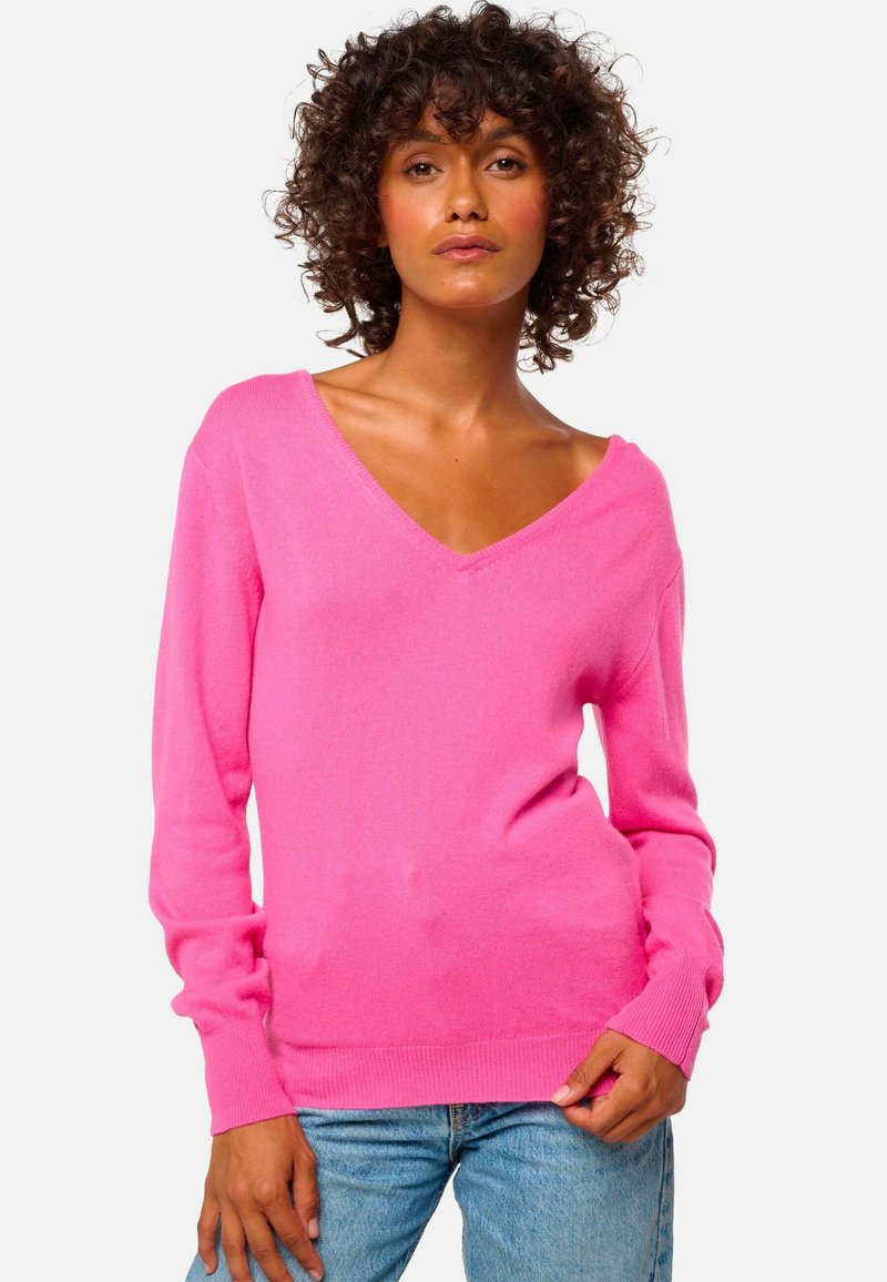 Pull en V rose en tissu doux, avec des manches longues et des poignets côtelés, porté avec un jean en denim bleu.