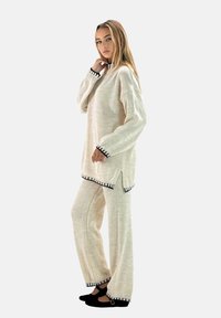 Suéter de punto beige claro y pantalones a juego con ribetes negros. Corte holgado, aberturas laterales en el suéter, puños y dobladillos acanalados. Textura suave.