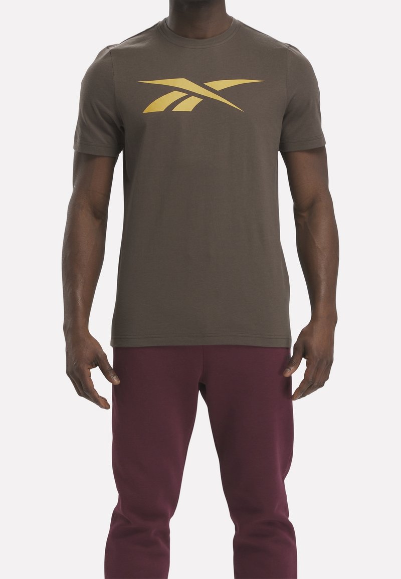 Camiseta de algodón marrón de manga corta con un prominente logo gráfico amarillo en el pecho. Diseño de cuello redondo simple, ajuste relajado.