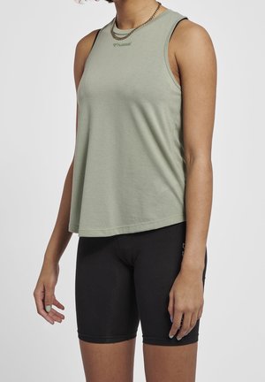 Woman wearing a sleeveless light green top and black biking shorts, shown from shoulders to mid-thigh against a plain background.