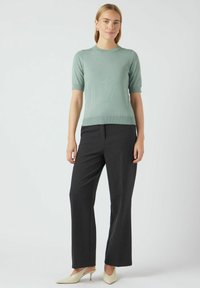 Svijetlozelena kratka pletena majica s kratkim rukavima u kombinaciji s crnim širokim hlačama koje ističu struk i imaju suptilnu rebrovanu teksturu. Cipele u krem boji s špicastim vrhom.