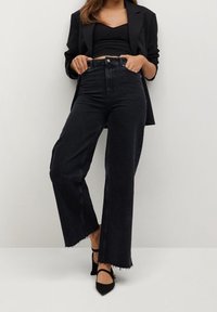 Jean en denim noir taille haute avec jambes droites, ourlet effiloché et design classique à cinq poches. Associé à un haut court noir et à un blazer.