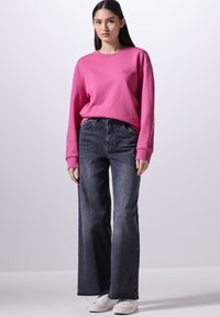 Felpa rosa con maniche lunghe e polsini a coste, abbinata a jeans a gamba larga grigio scuro a vita alta e sneakers bianche.