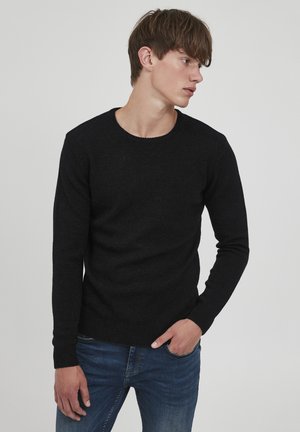 Zwart gebreid sweater met een ronde halslijn en geribbelde manchetten. Gladde textuur, aansluitend ontwerp, gedragen over blauwe jeans.