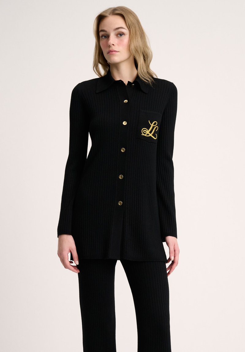Black ribbed cardigan with gold buttons, collared design, and left chest pocket featuring embroidered logo detail. Long-sleeve style.