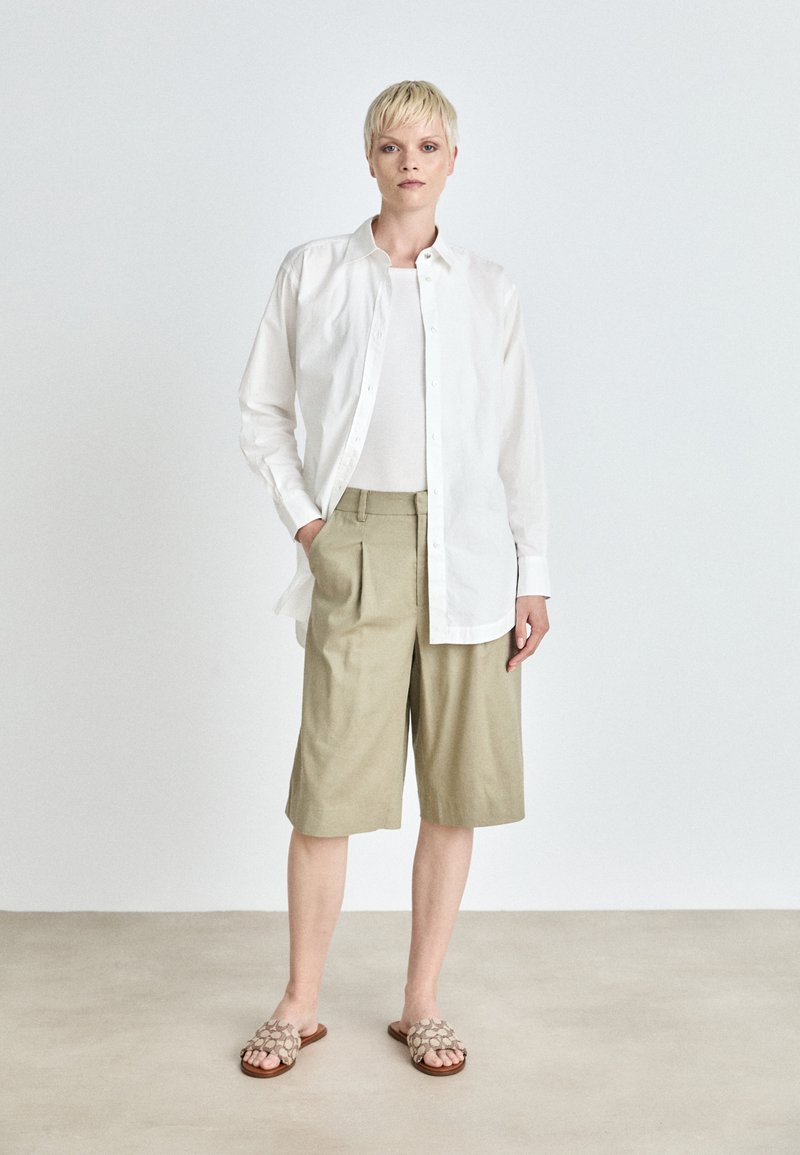 Witte button-up shirt, beige short tot de knie en tan gekleurde sandaaltjes met een patroon. Gladde stoffen en een relaxte pasvorm met geplooide shorts voor extra detail.