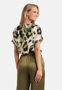 Korte mouwen top in een groen en beige luipaardprint met een sleutelgatdetail aan de achterkant, gecombineerd met olijfgroene losse broek.
