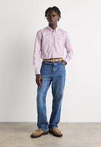 Camisa de botones a rayas rojas y blancas, jeans azules, cinturón marrón y zapatos marrones con suelas texturizadas. Diseño minimalista, materiales naturales.