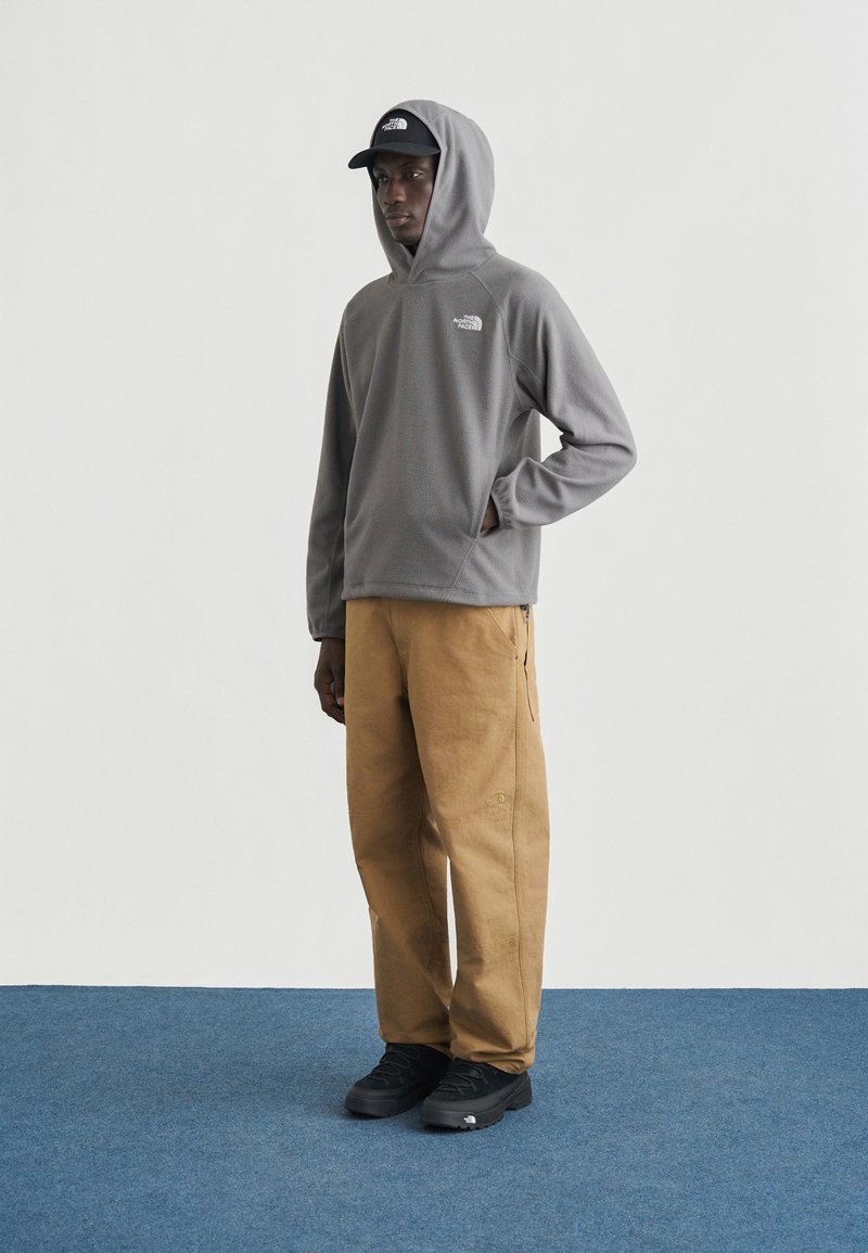 Gray fleece pullover hoodie with kangaroo pocket, paired with tan cargo pants and black footwear, standing on a blue carpet background.