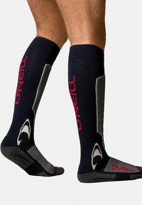 Kniesokken in marineblauw en grijs met een rood "O'Neill"-logo. Voorzien van een versterkte teen en hiel, een textuurdesign voor grip, en een contrasterende accenten.