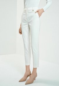 Białe dopasowane spodnie o wąskim kroju, z zamkiem błyskawicznym, szlufkami na pasek i kieszeniami. Połączone z cielistymi szpilkami z ostrym noskiem.