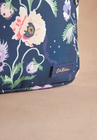 Sötétkék virágmintás textiltáska, világos rózsaszín és lila mákvirág mintákkal, texturált felülettel, és egy látható kék címkével, amelyen a "Cath Kidston" felirat olvasható.