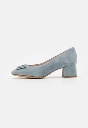 Pompe en suede bleu avec un bout arrondi, un talon carré et une boucle décorative sur le devant. Texture lisse et semelle de couleur claire.