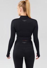 Čierny športový set pozostávajúci z dlhého crop topu s vysokým golierom a priliehavých legín s širokým pásom a logom.