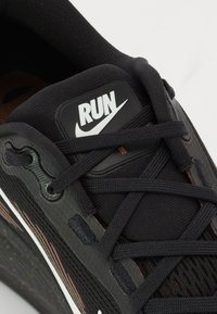Black Nike running shoe close-up with textured fabric, round laces, and a rectangular "RUN" tag in white on a black background.