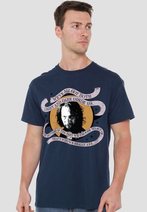 Man wearing navy blue T-shirt with black and white face and text about light and dark inside on yellow circle background.
