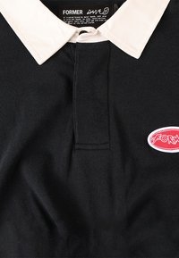 Black polo shirt featuring a contrasting white collar, a front placket, and a red oval logo patch with white text on the left side.