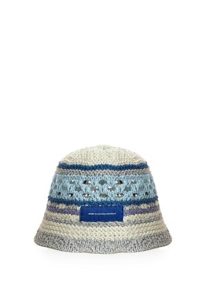 Sombrero tipo bucket de ganchillo con rayas blancas, azules y grises y una etiqueta azul en la parte delantera, con detalles de punto abierto cerca de la parte superior.