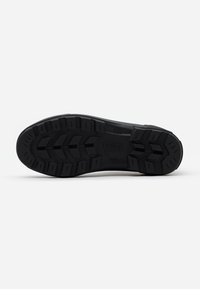 Black shoe sole with a textured rubber surface, featuring deep treads for traction and the brand name "Aigle" embossed in the center.