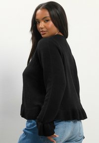 Musta neulottu villapaita, jossa on ribbireunat ja hihansuut, ja jossa on rakenteellinen kangas. Yhdistetty vaaleansinisiin farkkuihin.