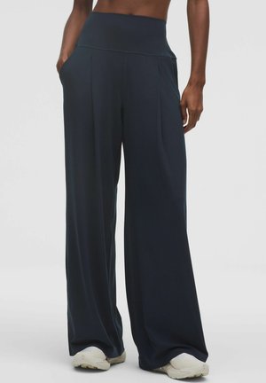 Spodnie o szerokich nogawkach w ciemnonawowym materiale, z wysokim stanem, kieszeniami bocznymi oraz gładką fakturą z delikatnymi plisami.