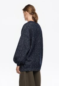 Granatowy sweter w kropki, okrągłym dekolcie i bufiastych rękawach. Wykonany z teksturowanej dzianiny, luźny krój, widok z tyłu.