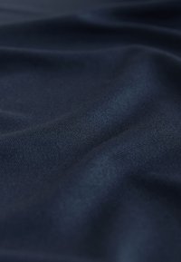 Tessuto blu navy scuro con trama a maglia fine visibile e pieghe morbide che creano ombre e riflessi sottili.