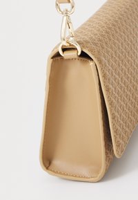 Beige faux lærveske med preget logo-mønster, gullfarget detaljer og en strukturert form. Har en avtakbar reim for allsidighet.