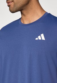 Camiseta azul de manga corta confeccionada con un tejido texturizado. Cuenta con un logo blanco en la parte superior izquierda del pecho y un cuello redondo.