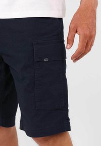 Shorts cargo navy en tissu résistant, avec des poches latérales, un ourlet cousu et une étiquette de logo "Oxbow" sur la poche.