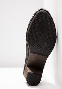 Semelle de chaussure en cuir noir avec grip en caoutchouc texturé, talon en bois et clous métalliques le long des bords, vue de dessous.