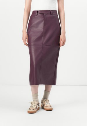 Woman wearing a fitted, high-waisted dark purple leather midi skirt with beige socks and patterned beige sneakers, standing against a white background.
