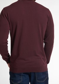 Pull à manches longues bordeaux en tissu doux, avec un col ras du cou et des poignets côtelés, associé à un jean en denim bleu foncé.